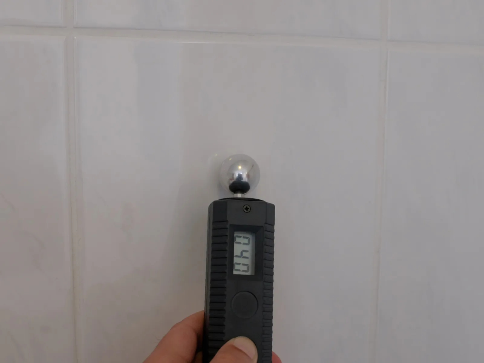 Moisture meter being used against a tiled wall during a damp survey